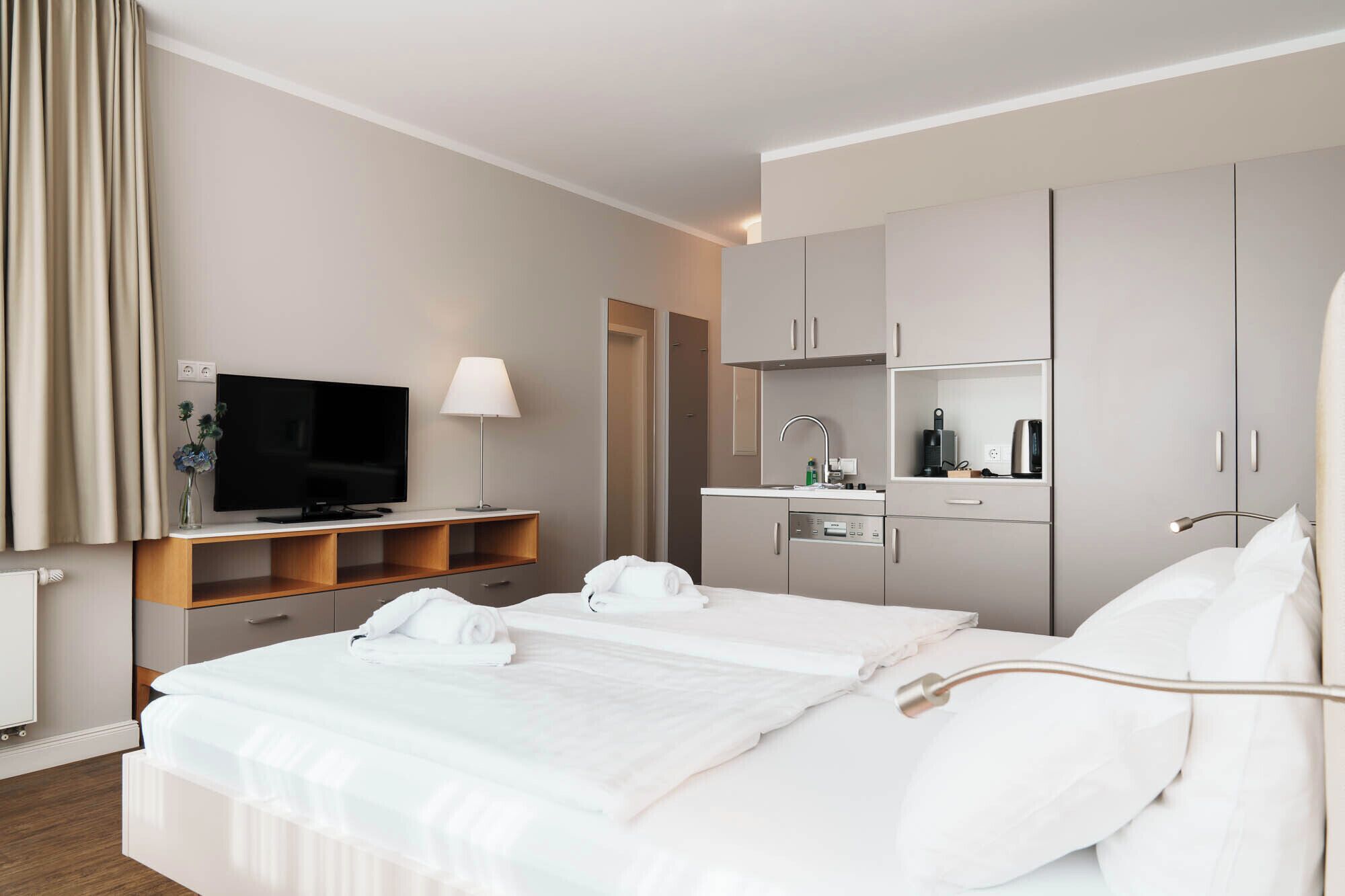 Een moderne hotelkamer met een bed, een televisie, een bureau met een lamp, een minibar en een badkamer.