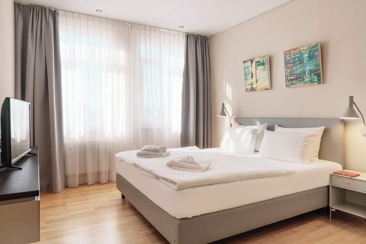 A hotel room with a large bed, a desk with a flat-screen TV, and two paintings on the wall.