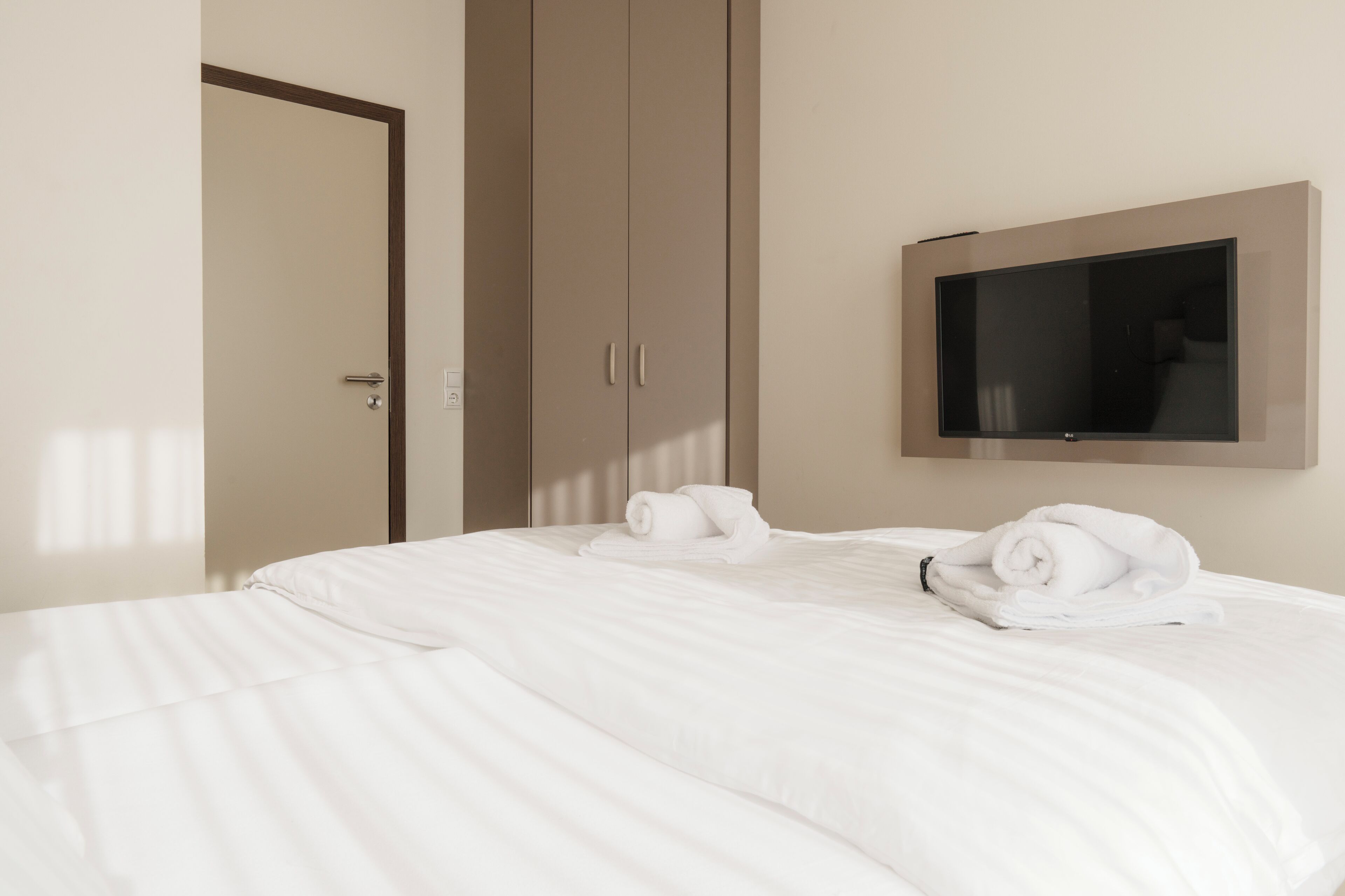 A hotel room with a bed, a wardrobe, and a flat-screen TV mounted on the wall.
