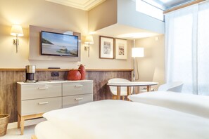 Habitación de hotel con cama, escritorio, silla, televisor y lámpara de pared.