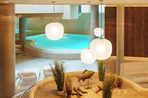 Ein moderner Innenpoolbereich mit Liegestühlen, einem zentralen Pool und Zierpflanzen.