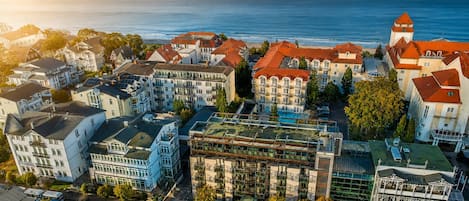En kystby med en blanding af boliger og erhvervsbygninger, herunder et markant hotel med rødt tag og et tårn.