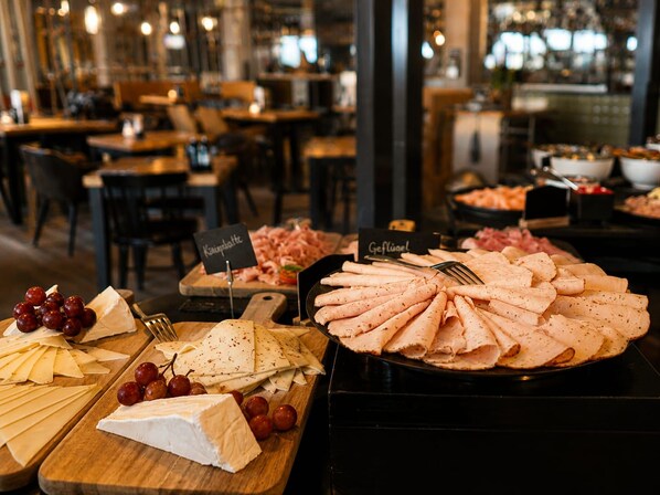 Un bufé con varios quesos, carnes y frutas.