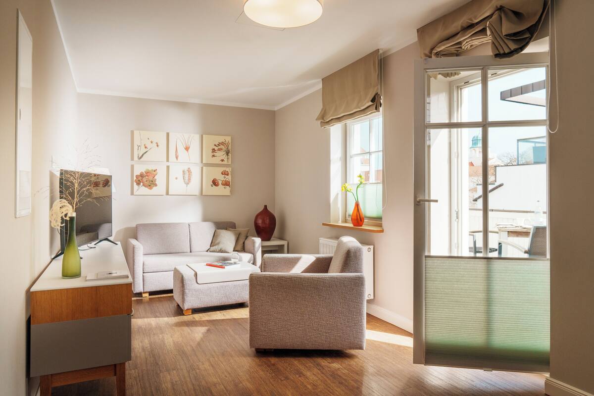 A modern living room with a sofa, armchair, and a coffee table. There is a vase on a side table and artwork on the wall.