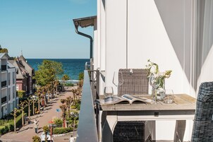 Ein Balkon mit Meerblick, ein Korbstuhl und ein Tisch mit einem Buch und Gläsern.