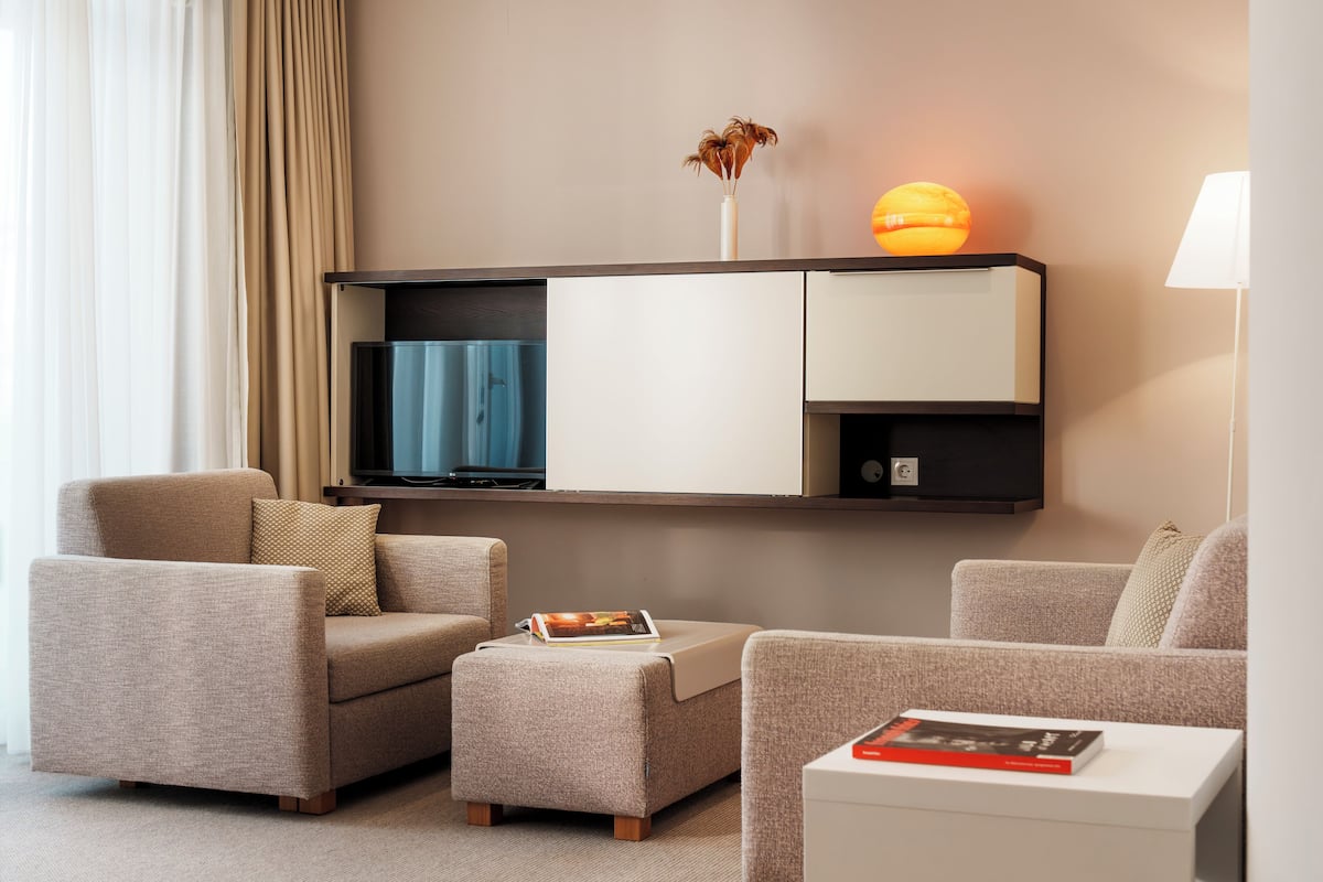 A modern living room with a sofa, ottoman, and a flat-screen TV mounted on the wall.