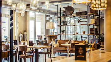 A cozy cafe with wooden tables and chairs, a sofa, and various decorative items on shelves.