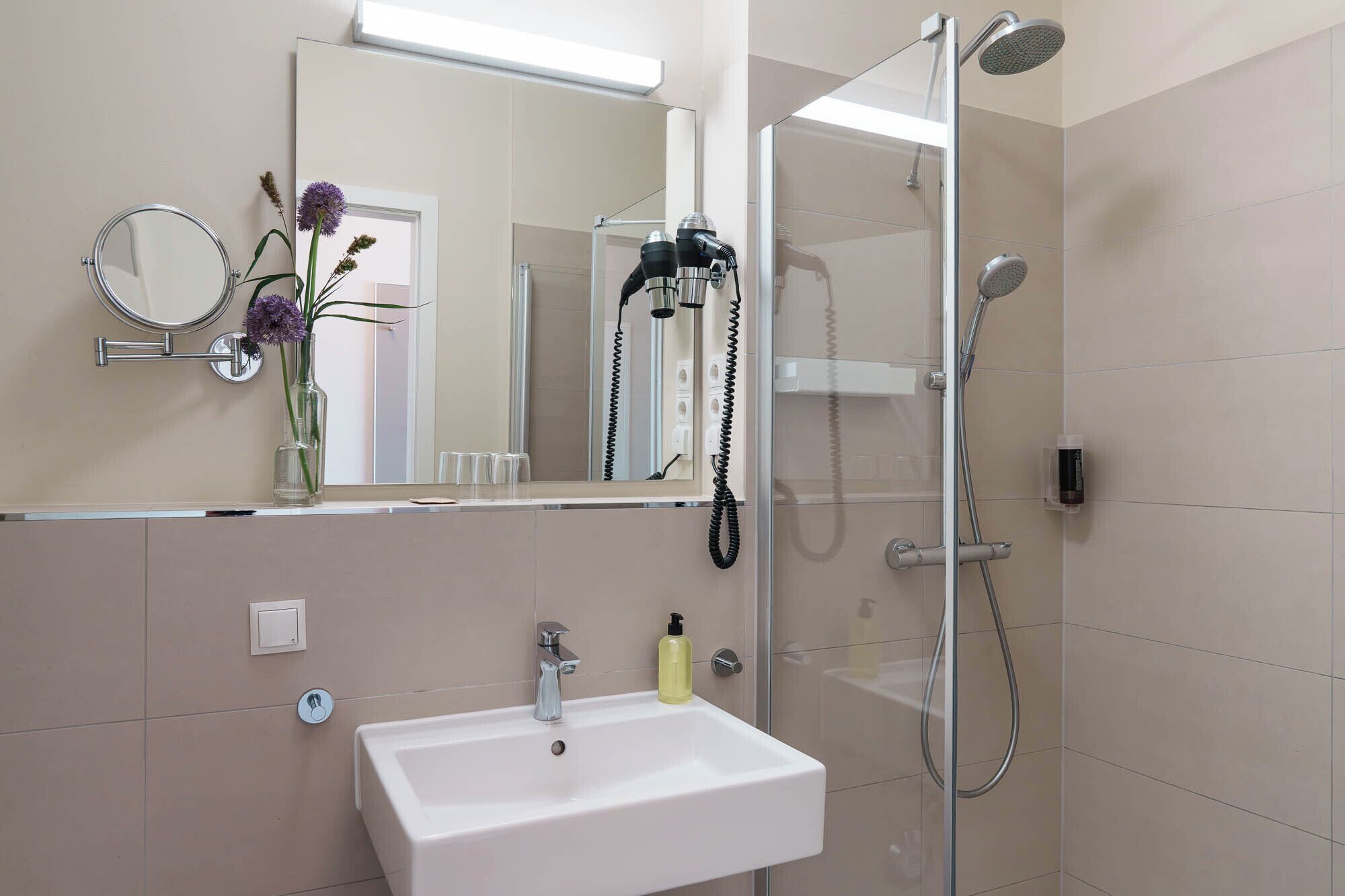 Un baño moderno con un lavamanos blanco, un cabezal de ducha de mano y un espejo con marco redondo.
