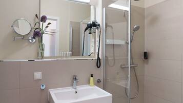 Un baño moderno con un lavamanos blanco, un cabezal de ducha de mano y un espejo con marco redondo.