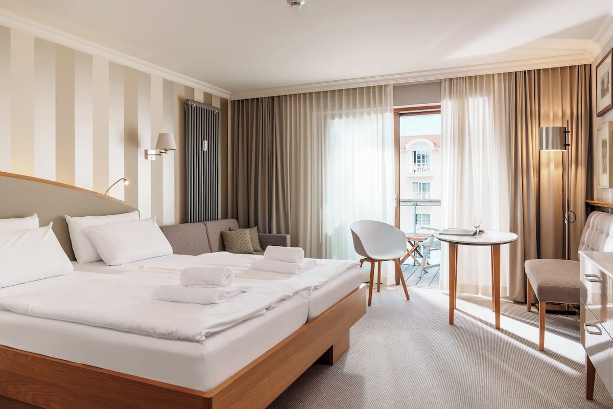 A hotel room with a large bed, a seating area with a table and chairs, and a view of the outside.