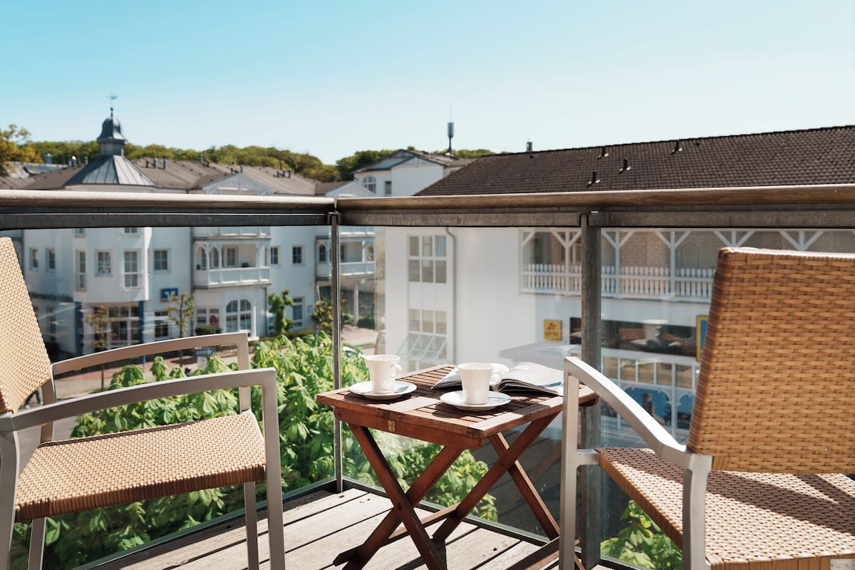 A balcony with wicker chairs, a small table, and a view of buildings.