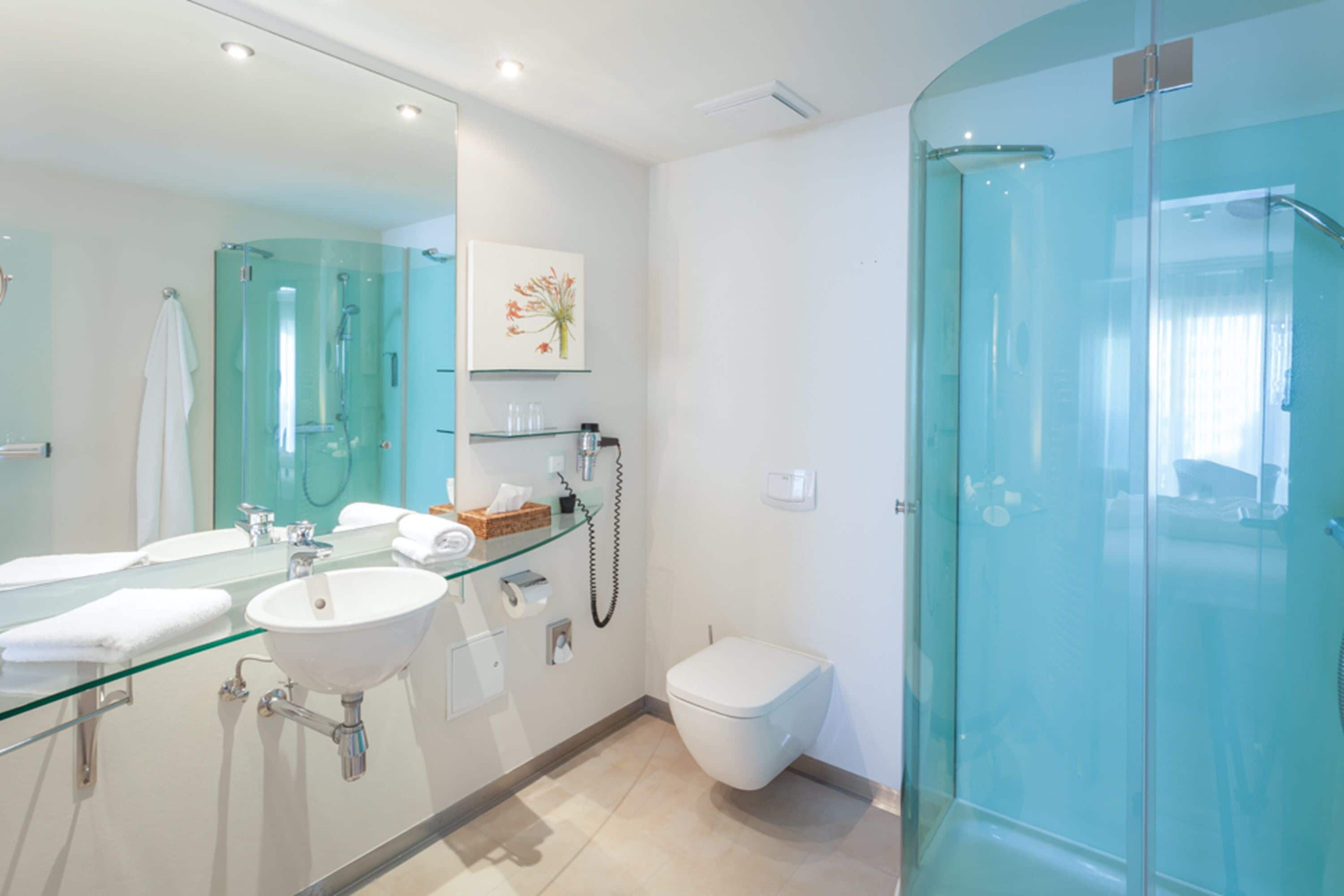Un baño moderno con ducha envuelta en vidrio, lavamanos blanco y un espejo grande.