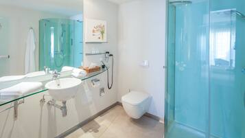 Un baño moderno con ducha envuelta en vidrio, lavamanos blanco y un espejo grande.