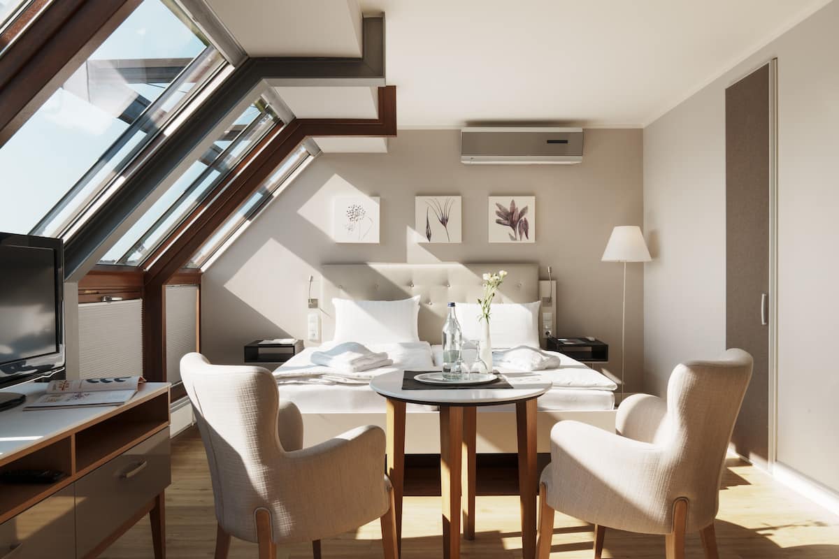 A modern hotel room with a skylight, a bed, a desk, and two chairs.