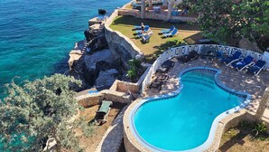 Ein Poolbereich mit Steinrand, Liegestühlen und Blick auf das Meer.