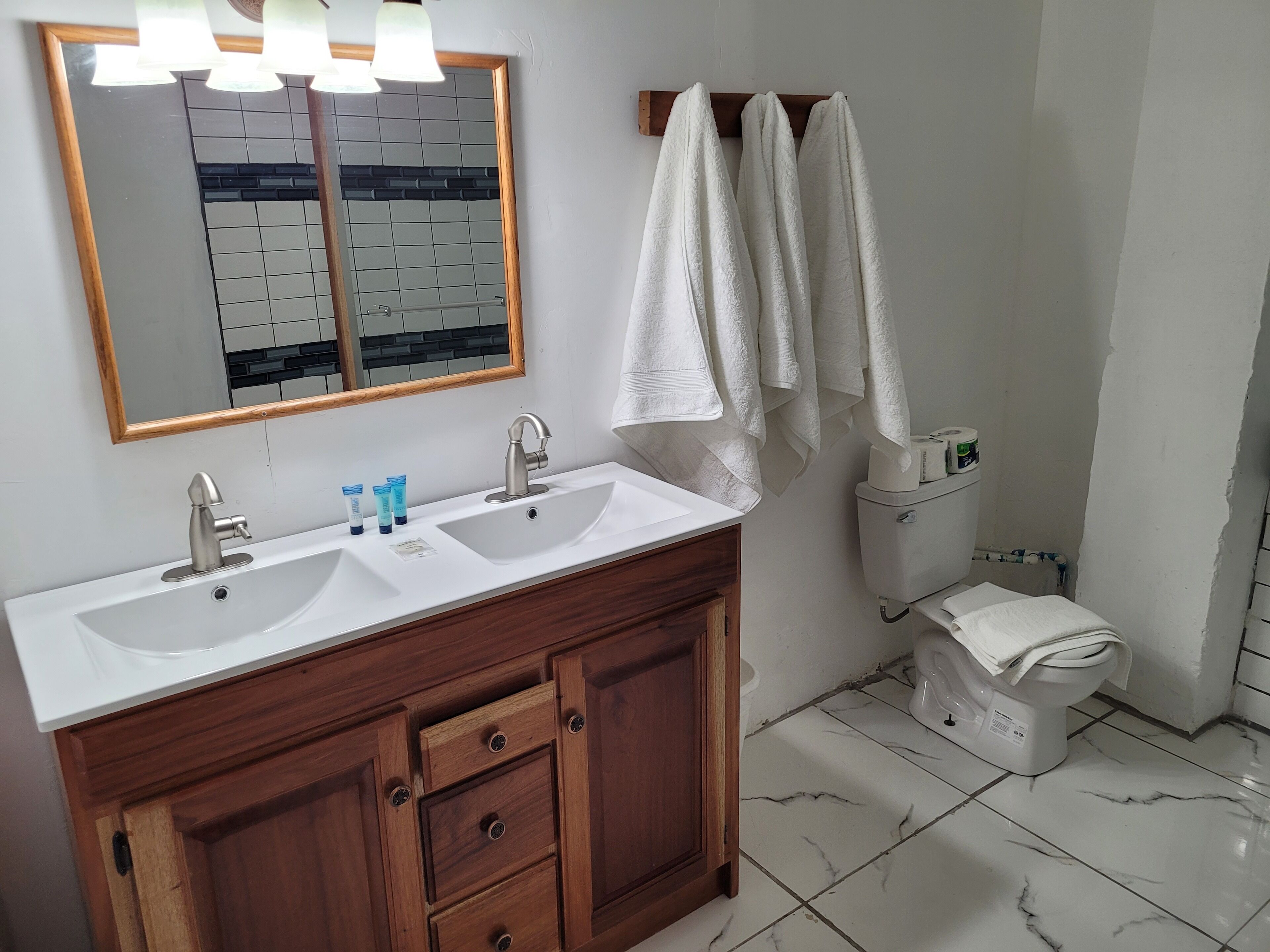 Un baño con tocador de madera, dos lavamanos, un espejo con iluminación y un inodoro.