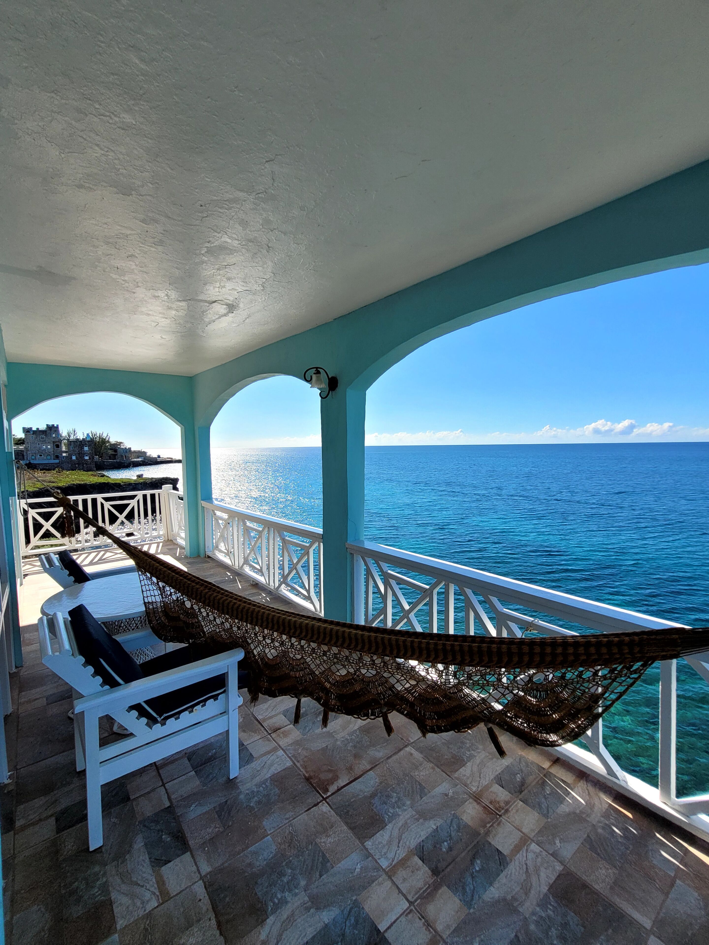 A balcony with a hammock, white chairs, and a view of the ocean.