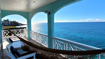 A balcony with a hammock, white chairs, and a view of the ocean.