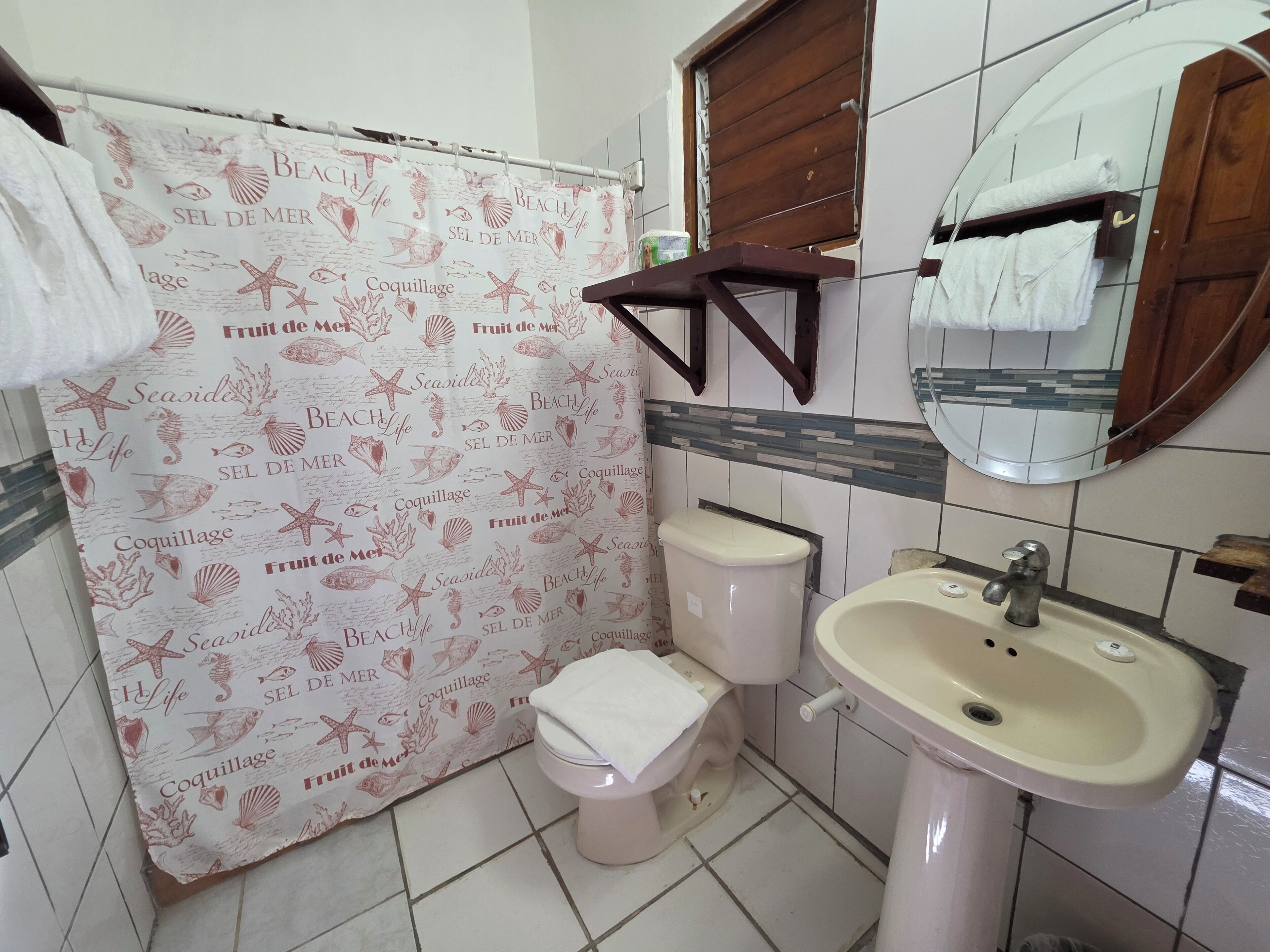 Casa de banho com sanita, lavatório, espelho e cortina de chuveiro com motivos náuticos.