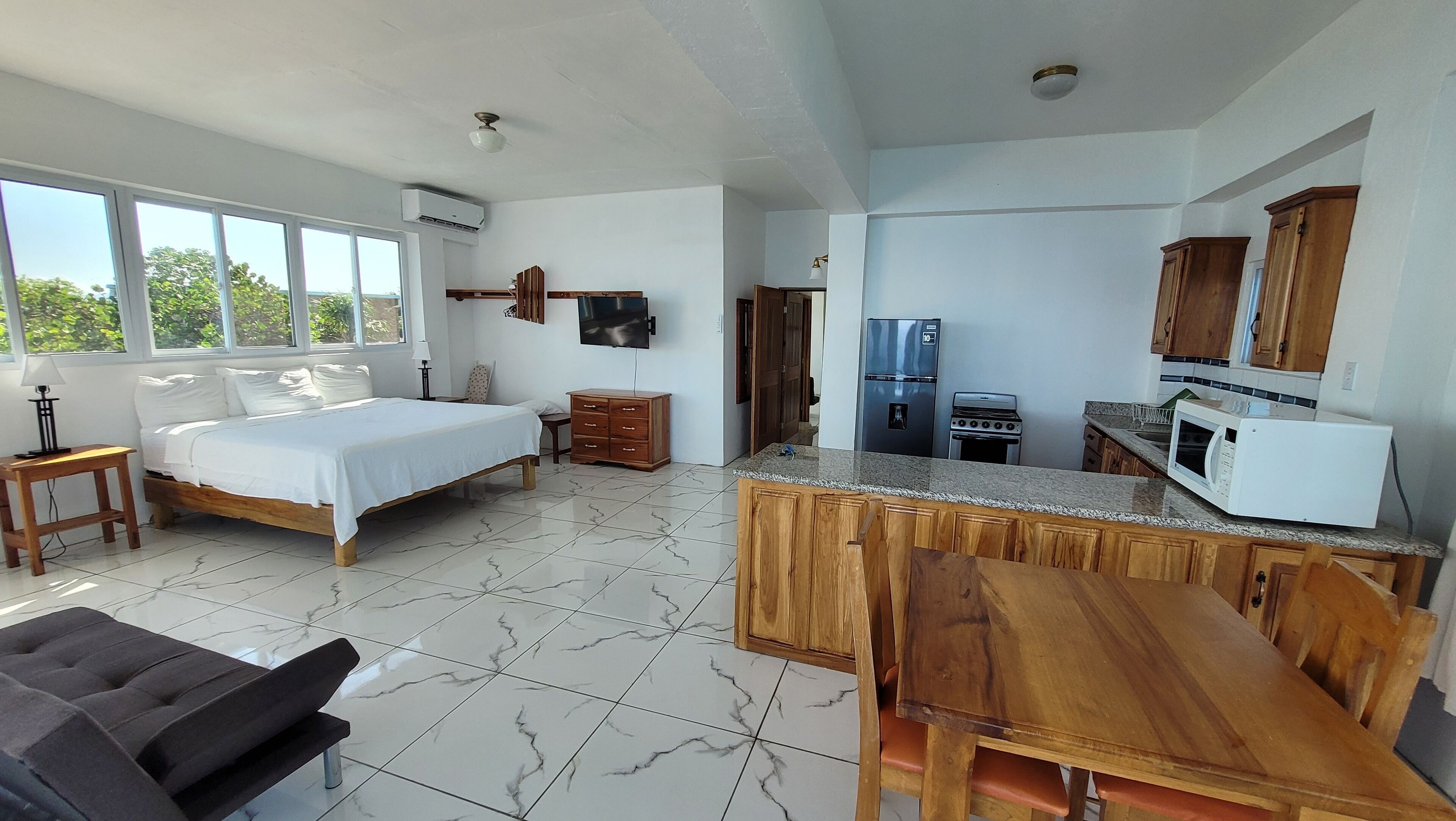 A bedroom with a bed, bedside table, and a window. The room has a tiled floor and a ceiling fan.