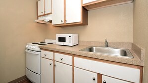 A compact kitchen with white cabinets, a microwave, a stove, and a sink. - Extended Stay America - Houston - Northwest (Houston)