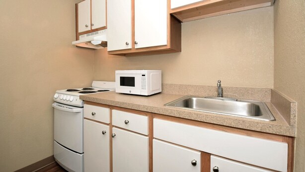 A compact kitchen with white cabinets, a microwave, a stove, and a sink. - Extended Stay America - Houston - Northwest (Houston)