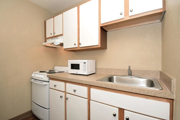 A compact kitchen with white cabinets, a microwave, a stove, and a sink. - Extended Stay America - Houston - Northwest (Houston)