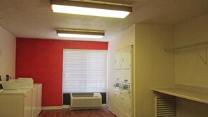A laundry room with a red wall, a window with blinds, a white heater, and a white drying rack. - Extended Stay America - Houston - Northwest (Houston)