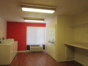 Un cuarto de lavandería con pared roja, una ventana con persianas, un calefactor blanco y un tendedero blanco.