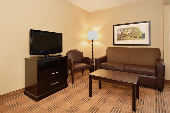 A hotel room with a flat-screen TV, a sofa, a coffee table, a lamp, and a framed picture on the wall. - Extended Stay America - Houston - Northwest (Houston)
