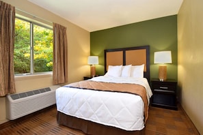 A hotel room with a bed, two bedside lamps, a window with curtains, and a wall-mounted heater. - Extended Stay America - Houston - Northwest (Houston)