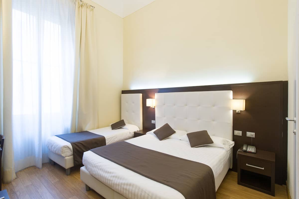 Ein Hotelzimmer mit zwei Betten, einem Nachttisch mit Lampe und einem Fenster mit Vorhängen.