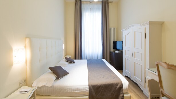 A hotel room with a bed, bedside table, lamp, wardrobe, and a television. - Hotel Cosimo De' Medici (Florence)
