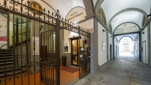A hotel corridor with a wrought iron gate, signs for the Fratelli Alinari Show Room, and a staircase leading to an upper floor. - Hotel Cosimo De' Medici (Florence)