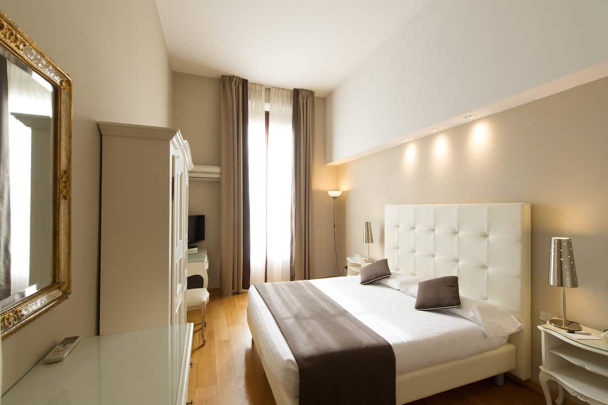 Ein modernes Hotelzimmer mit einem großen Bett, einem Nachttisch, einem Schreibtisch und einem Spiegel.