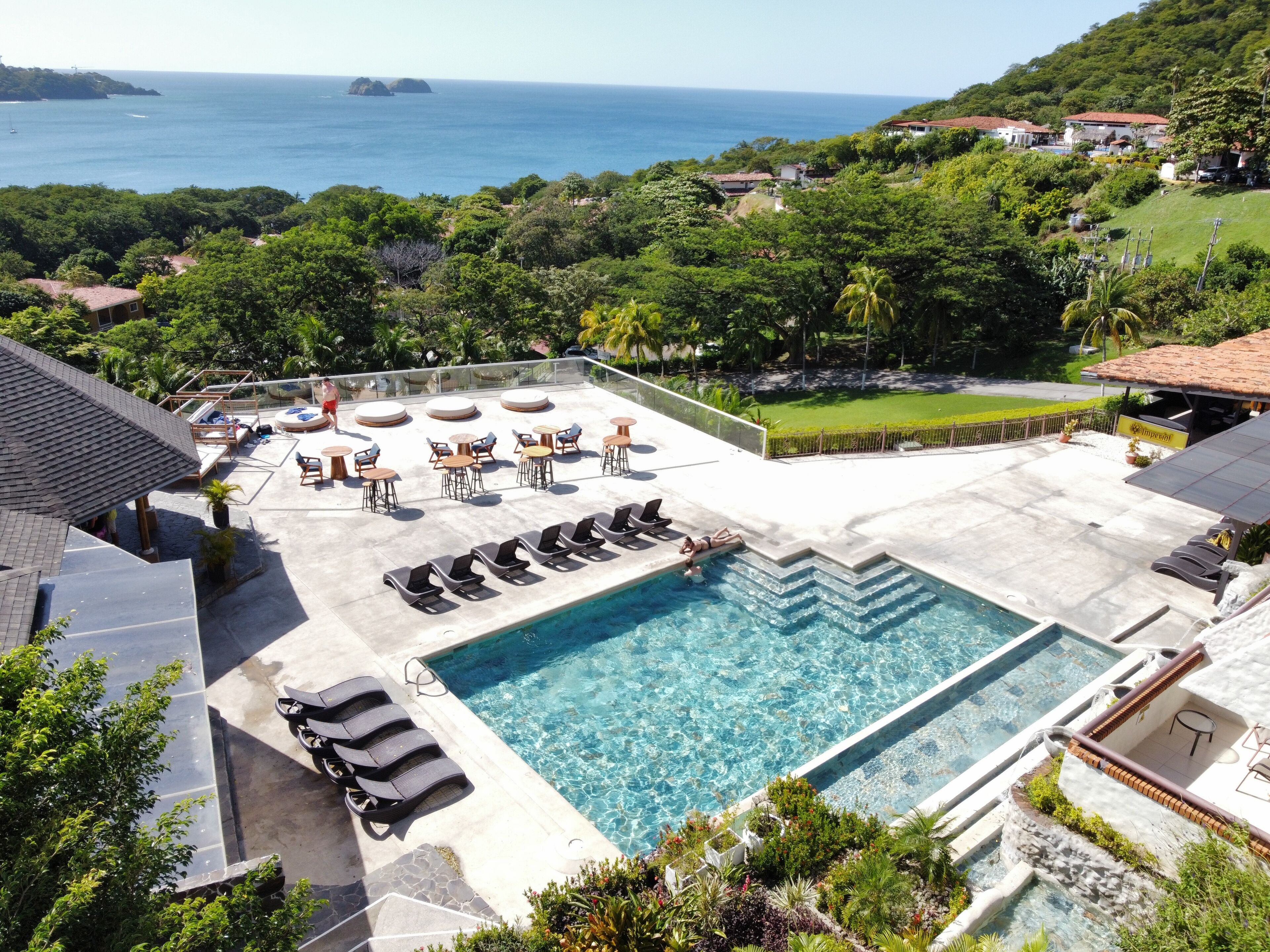 Uma área de piscina no terraço com água azul cristalina, rodeada por espreguiçadeiras e vista para o oceano.