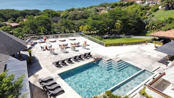 Uma área de piscina no terraço com água azul cristalina, rodeada por espreguiçadeiras e vista para o oceano.
