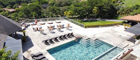 Zona de piscina en la azotea con agua azul cristalina, rodeada de sillones de descanso y vistas al océano.