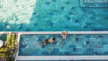 An aerial view of a rectangular swimming pool with a tiled edge, surrounded by greenery.