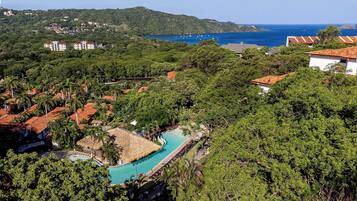 Un resort con piscina rodeada de exuberante vegetación y vista al mar.