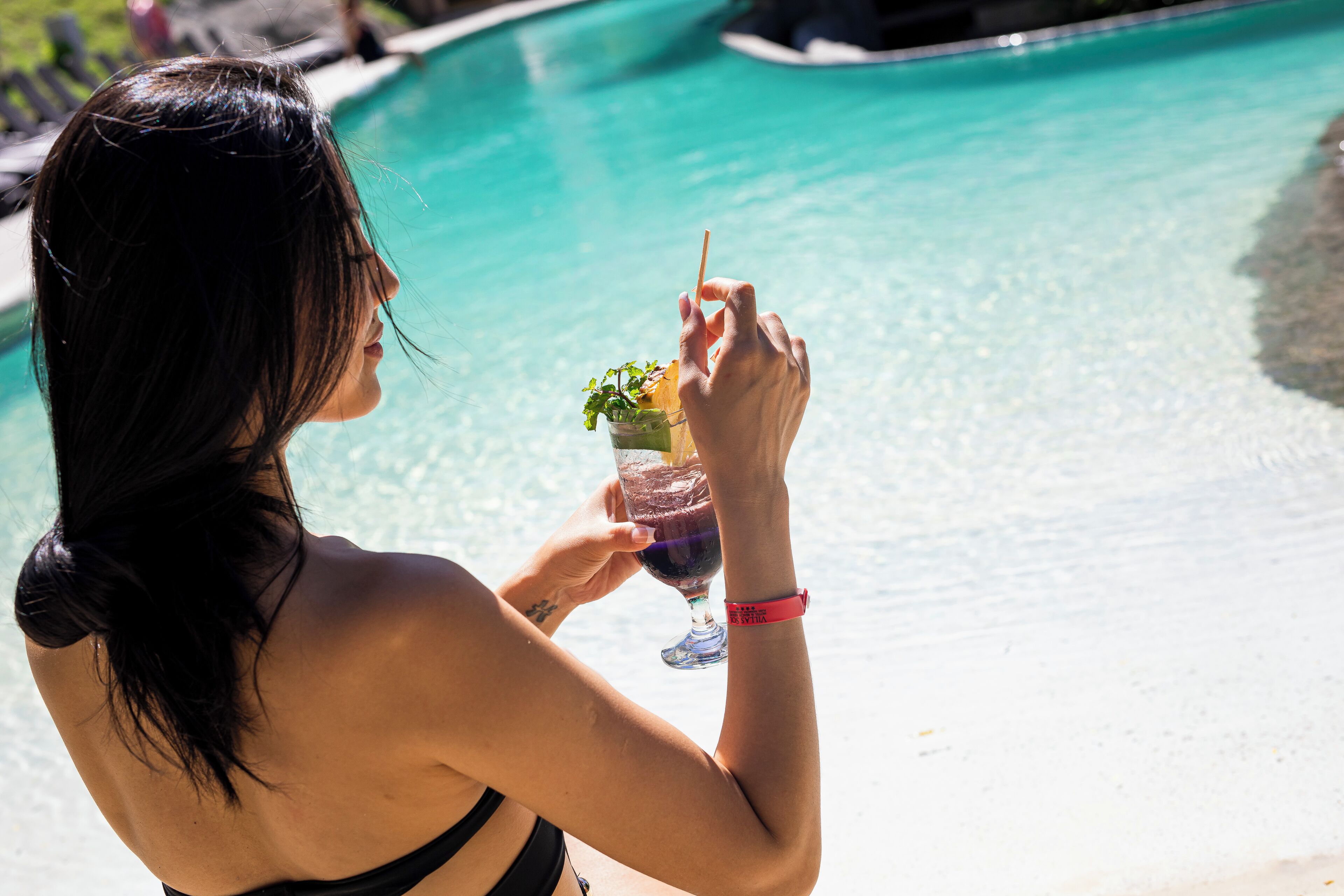 A person holding a drink by a pool.