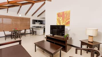 A modern living room with a wooden coffee table, a TV stand, and a dining area with chairs and a table.