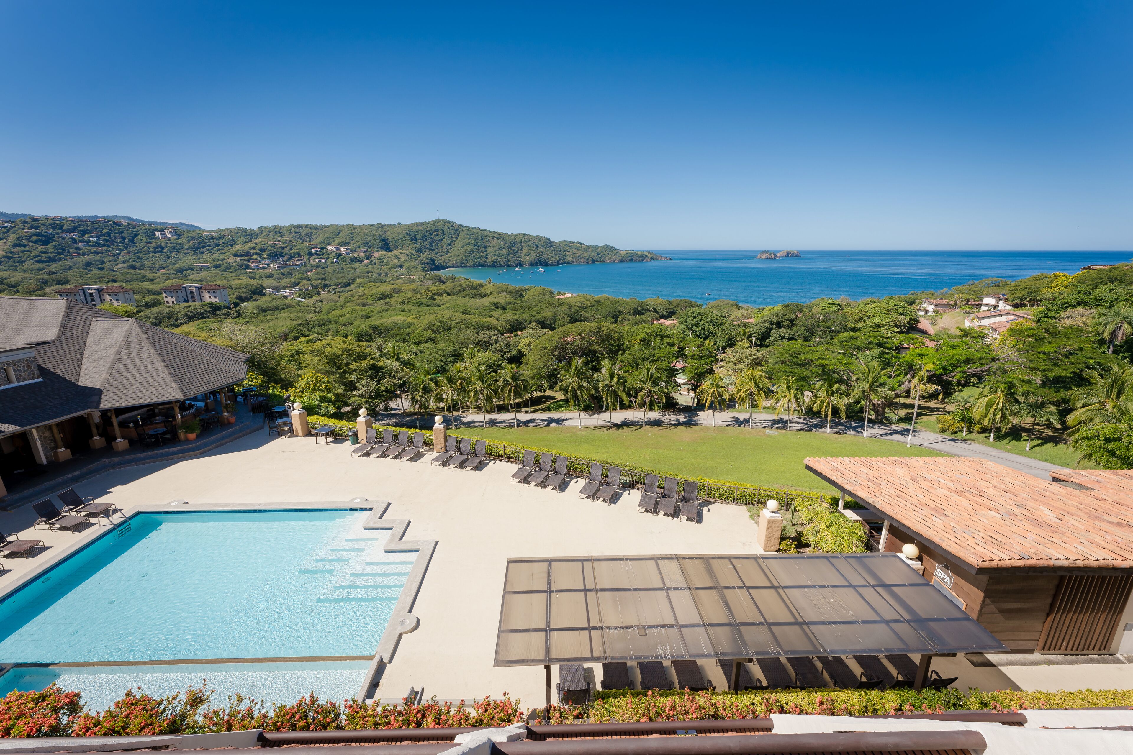 A resort with a swimming pool, sun loungers, and a view of the ocean.