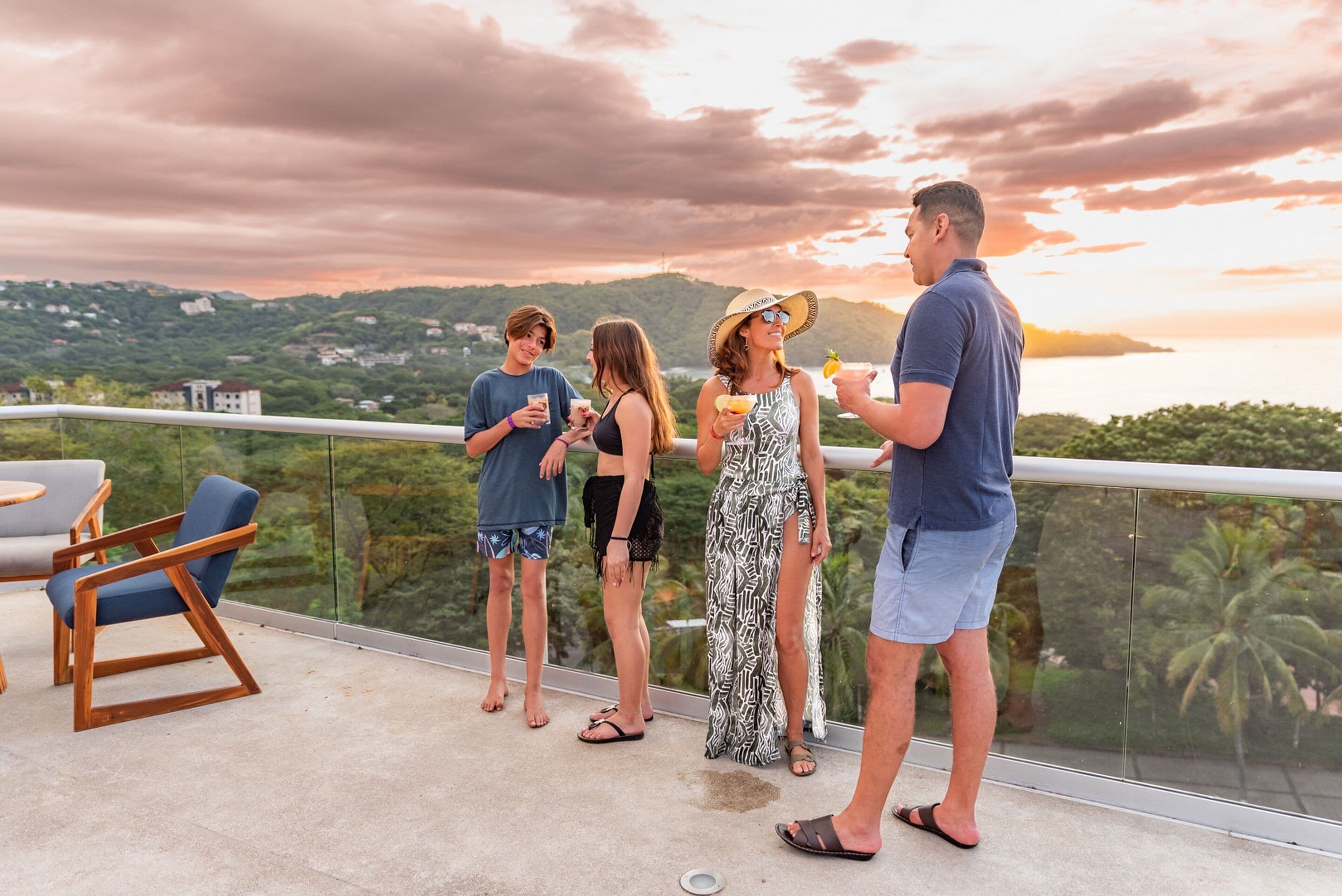 A group of people on a balcony with a scenic view of hills and a body of water.