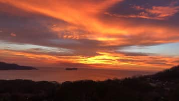 A sunset over a coastal landscape with silhouettes of trees and distant islands.