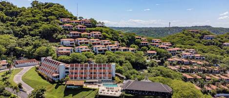 An aerial view of a residential area with multiple houses, a swimming pool, and a large building with a sloped roof.