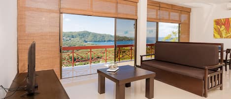 Un salon moderne avec un canapé, une table basse et un téléviseur posé sur un meuble. De grandes fenêtres offrent une vue sur un paysage pittoresque.