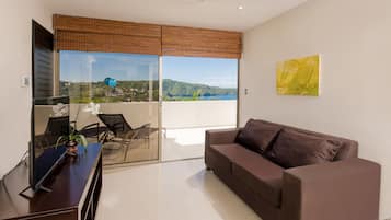 A modern living room with a brown sofa, a glass table, and a view of a lake and hills.