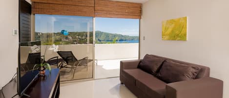A modern living room with a brown sofa, a glass table, and a view of a lake and hills.