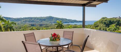 A round table with chairs on a balcony overlooking a scenic view of hills and a body of water.